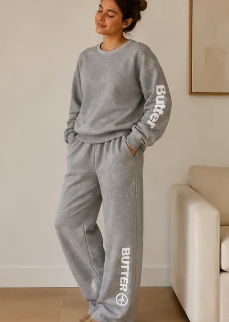 Model in a lifestyle setting wearing a heather grey crewneck sweatshirt and matching sweatpants set.