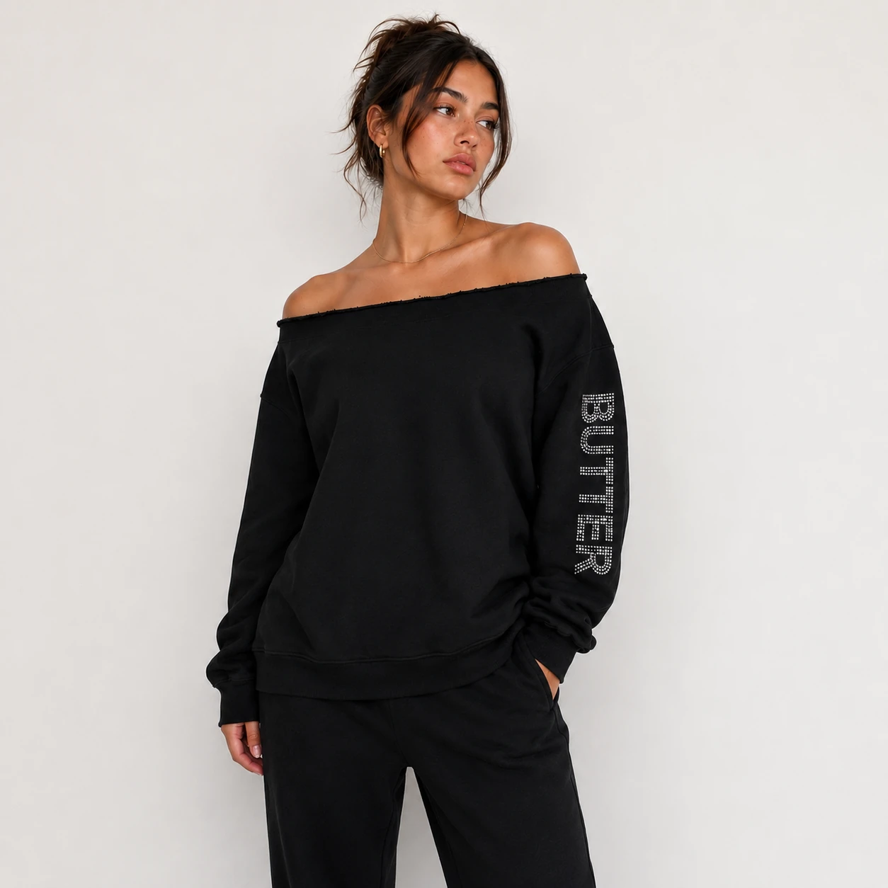 Model wearing a black off-the-shoulder sweatshirt and matching pants set with rhinestone details.
