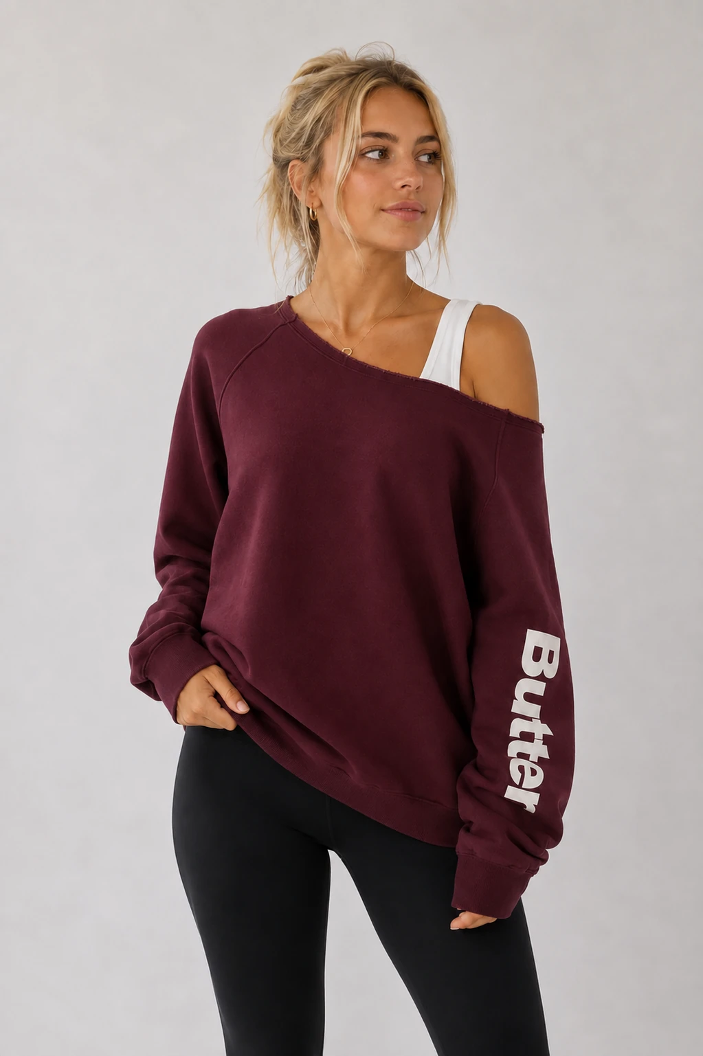 Burgundy/maroon off-the-shoulder sweatshirt with white 'Butter' text printed vertically on the left sleeve, worn by a model with black leggings.