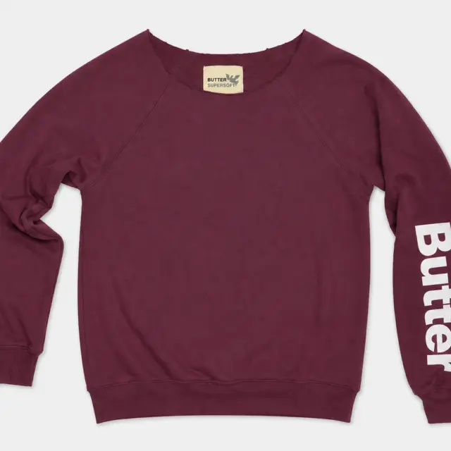 Burgundy off-the-shoulder sweatshirt with a white vertical logo on the left sleeve and raglan sleeve construction.