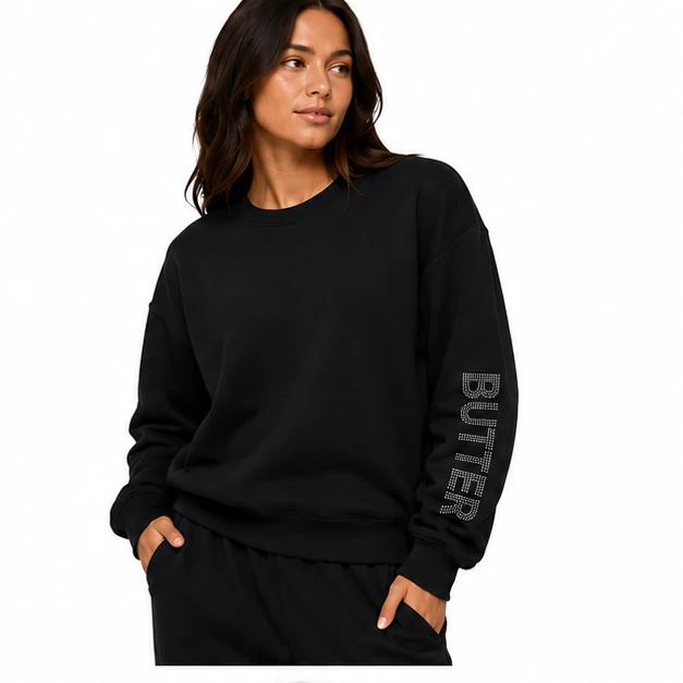 Model wearing a black crewneck sweatshirt featuring a textured 'BUTTER' logo on the sleeve.