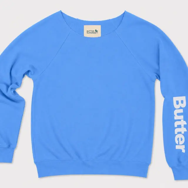 Bright blue off-the-shoulder sweatshirt with a white vertical logo on the left sleeve and raglan sleeve construction.