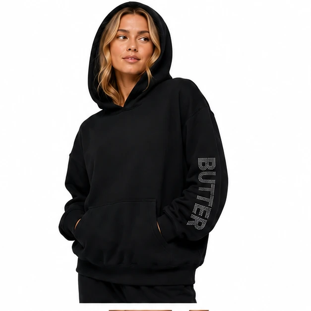 Model wearing a black pullover hoodie against a plain white background. The sleeve features a rhinestone 'BUTTER' logo.