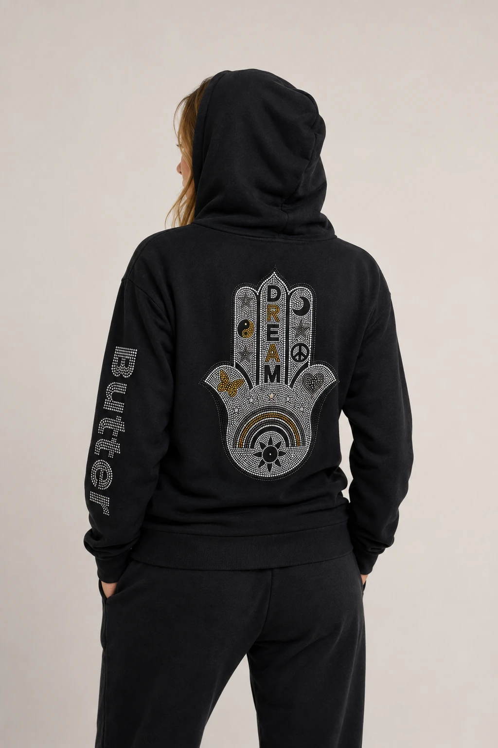 Rear view of a model wearing a black hoodie with the large Hamsa hand graphic visible on the back.